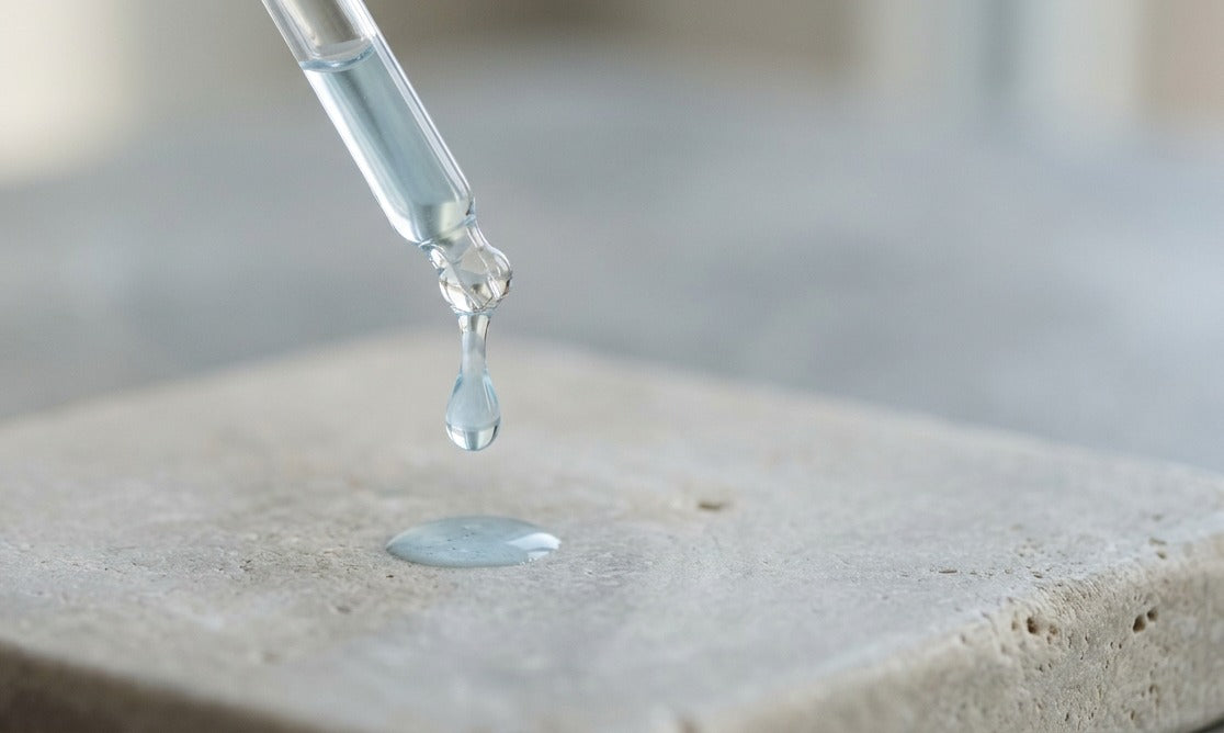 AI-generated image of a clear serum droplet falling from a glass dropper onto a stone surface